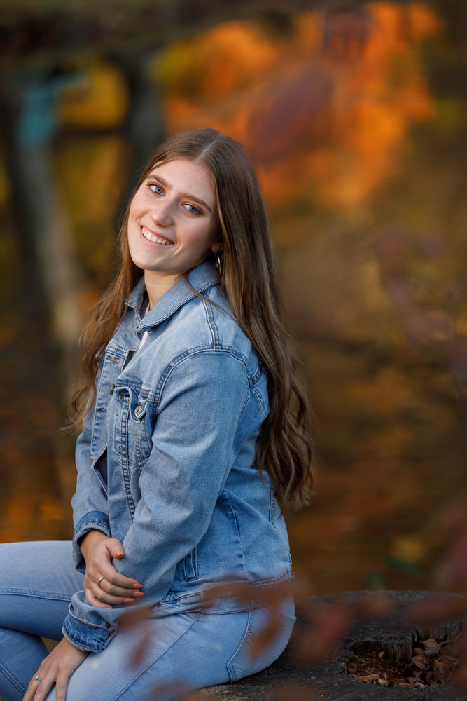 Fall foliage colors reflecting in water of background of senior girl in jean outfit